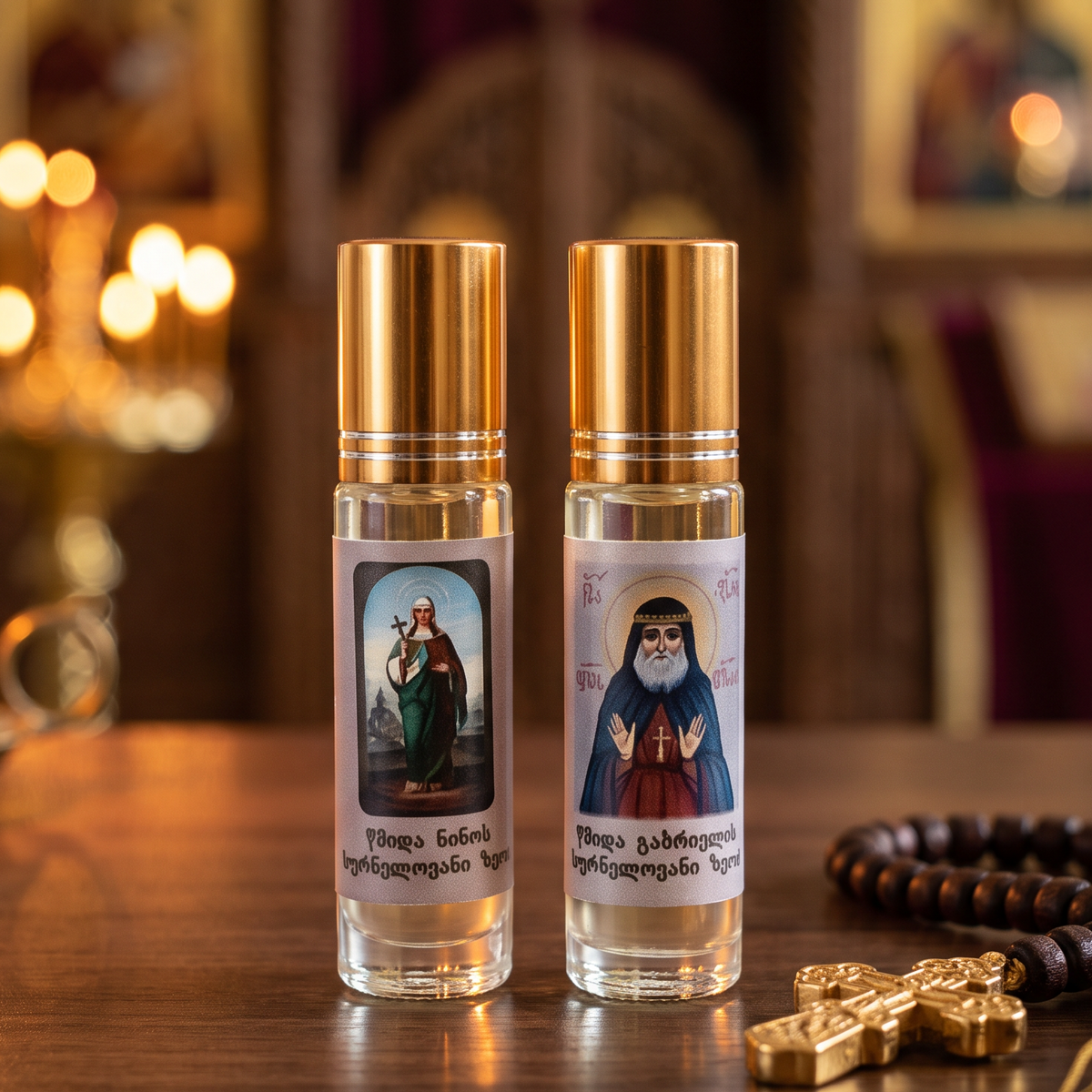 Two small clear glass bottles with gold caps, each containing a liquid and featuring a religious label with an icon, displayed on a wooden table alongside a gold cross, prayer beads, and a burning candle in a softly blurred church interior.